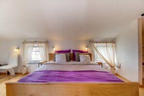 Um quarto com cama de madeira, cortinas brancas e colcha roxa.