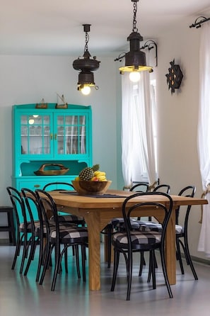 Uma sala de jantar com uma mesa de madeira rodeada por cadeiras pretas, um armário turquesa com portas de vidro e duas luminárias pendentes.