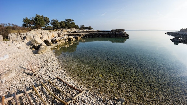 Un lac limpide et paisible, bordé d’une rive rocheuse et doté d’une jetée en pierre qui s’avance dans l’eau.