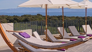 Une terrasse dotée de chaises longues et de parasols blancs, offrant une vue imprenable sur un paysage pittoresque, avec des arbres et des montagnes.