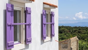 Un bâtiment aux murs blancs et aux volets violets, qui offre une vue sur un paysage côtier verdoyant et un ciel dégagé.