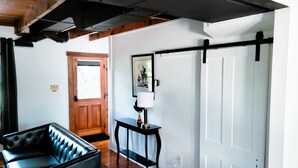 Ein modernes Interieur mit Holzbalkendecke, einem schwarzen Ledersofa, einem kleinen Tisch mit Lampe und einer weißen Tür.