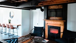 Ein modernes Wohnzimmer mit freiliegenden Holzbalken, einem Kamin und einem Essbereich mit Stühlen und einem Tisch.