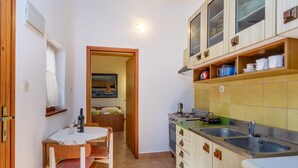 A compact kitchen with wooden cabinets, a dining table with chairs, and a painting on the wall. - Apartment casa MELITA with garden near Pula (Štinjan)