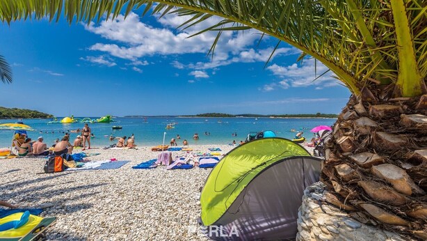 A beach with people sunbathing, swimming, and playing in the water. There are tents and umbrellas on the sand. - Apartment casa MELITA with garden near Pula (Štinjan)