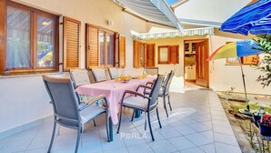 A patio with a table set for four, surrounded by chairs, and a colorful umbrella. - Apartment casa MELITA with garden near Pula (Štinjan)