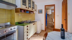 A compact kitchen with a stove, sink, and cabinets, leading to a bathroom with a shower. - Apartment casa MELITA with garden near Pula (Štinjan)