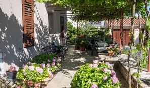 A narrow pathway lined with potted plants and a bench, leading to a building with a brown shutter and a small window. - Apartment casa MELITA with garden near Pula (Štinjan)