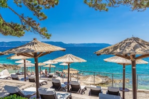 A beachside lounge area with umbrellas and lounge chairs, overlooking the sea.