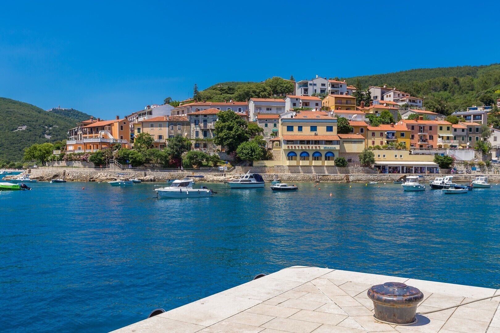 Une ville côtière aux bâtiments aux couleurs vives, un port de plaisance rempli de bateaux et un ciel d’un bleu limpide.