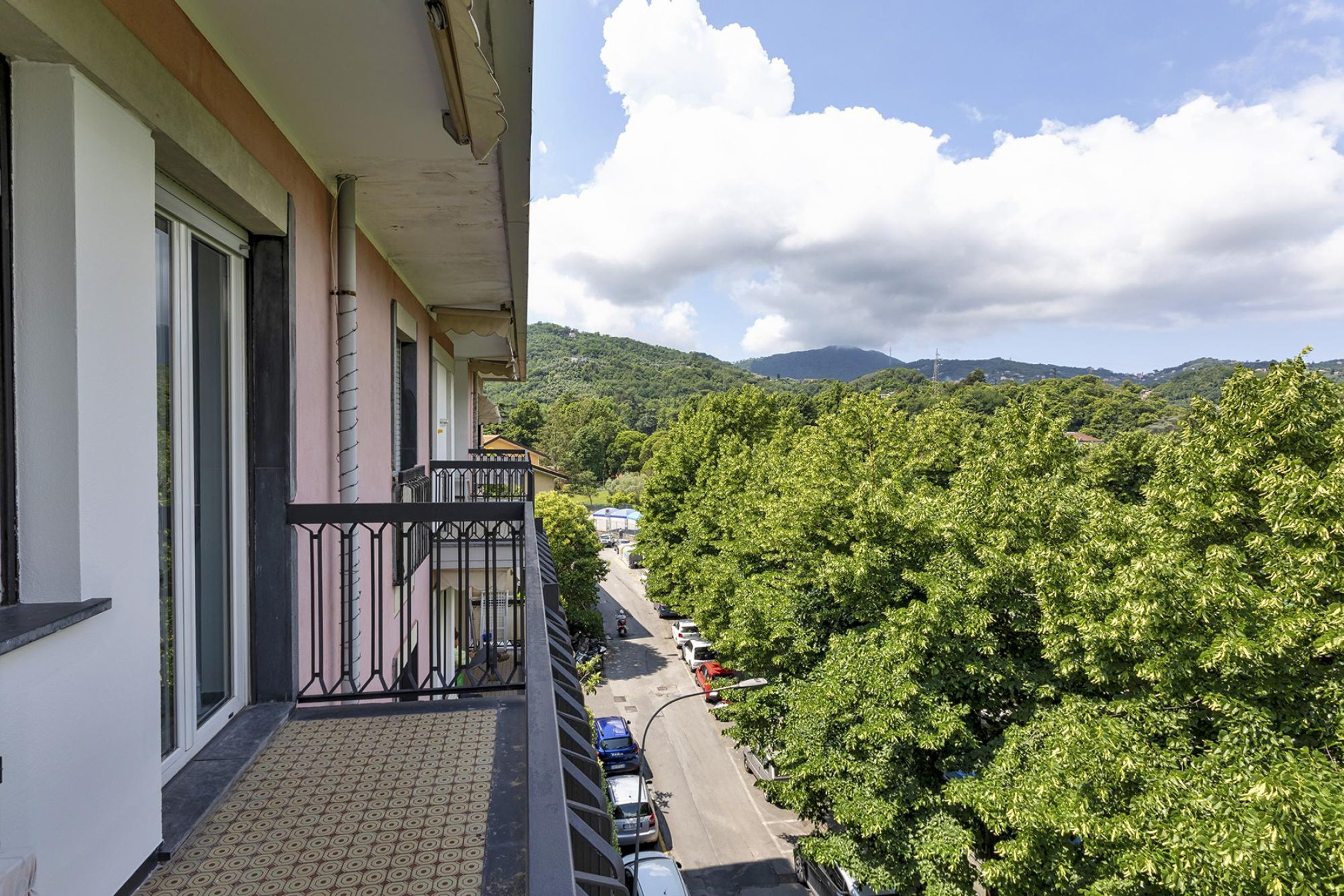 A balcony with a view of a tree-lined street and distant hills.
