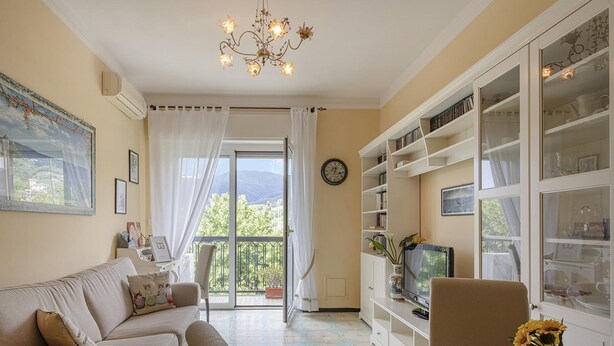 A living room with a sofa, a television, and a bookshelf. There is a large window with a view of greenery and mountains. - Un Balcone Sulle Colline di Rapallo by Wonderful Italy (Rapallo)