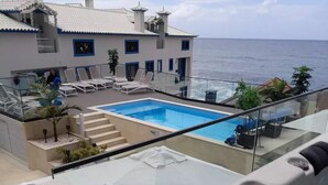 Une piscine sur le toit, dotée d’une balustrade en verre, de chaises longues et offrant une vue sur la mer.