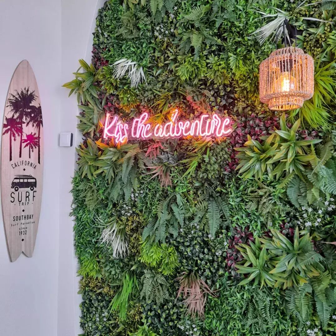 Un mur décoré d’une variété de plantes et un panneau néon sur lequel on peut lire : « Embrassez l’aventure ».