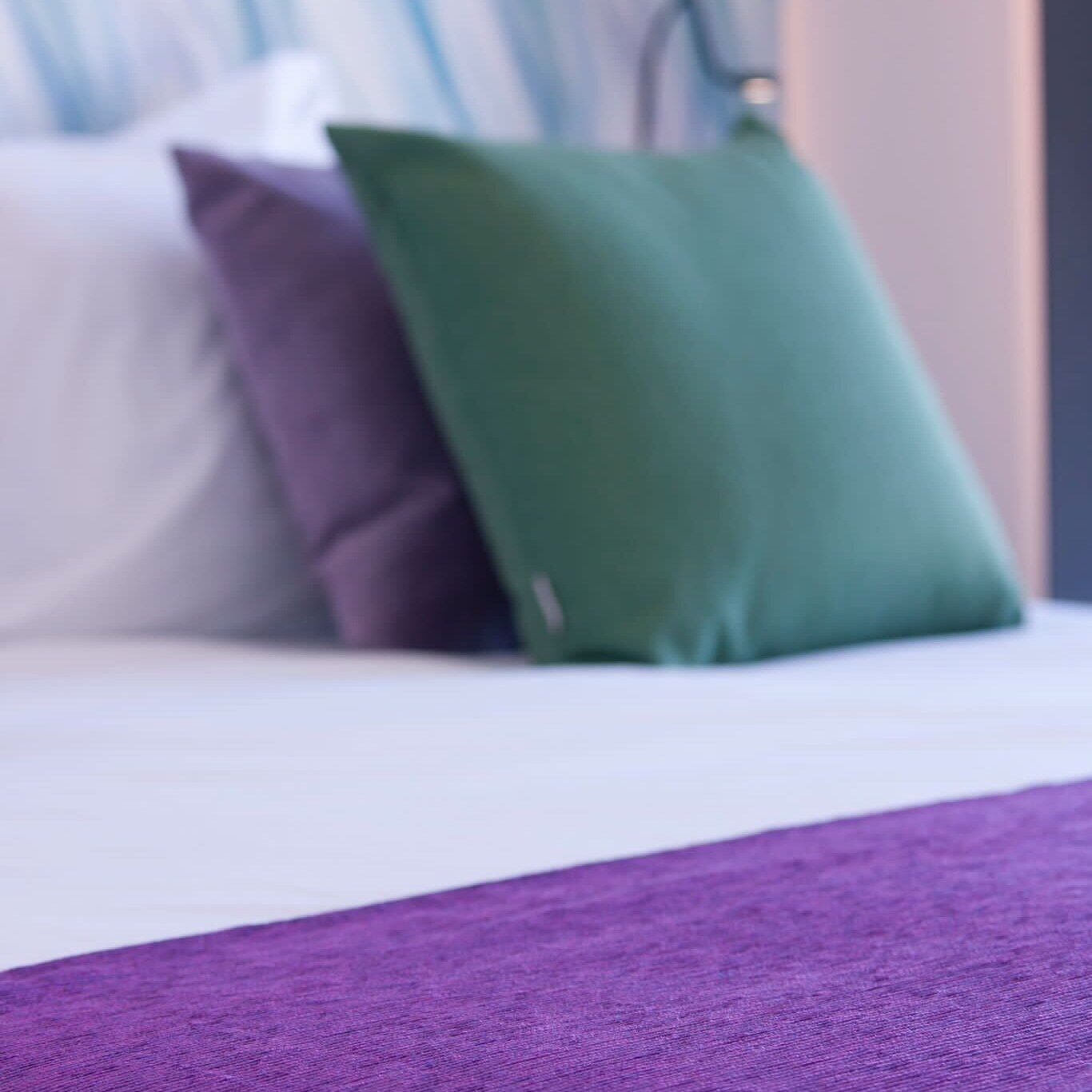 Una cama con un edredón morado y dos almohadas, una verde y otra morada.