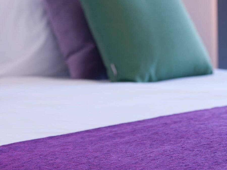 Una cama con un edredón morado y dos almohadas, una verde y otra morada.