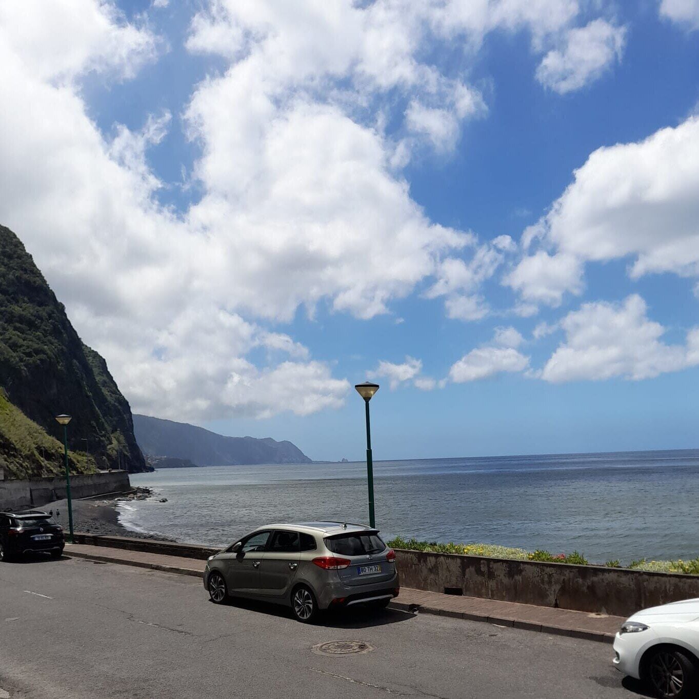 Una carretera costera con un coche estacionado, una farola y vistas al océano y montañas.