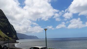 A coastal road with a parked car, a street lamp, and a view of the ocean and mountains.