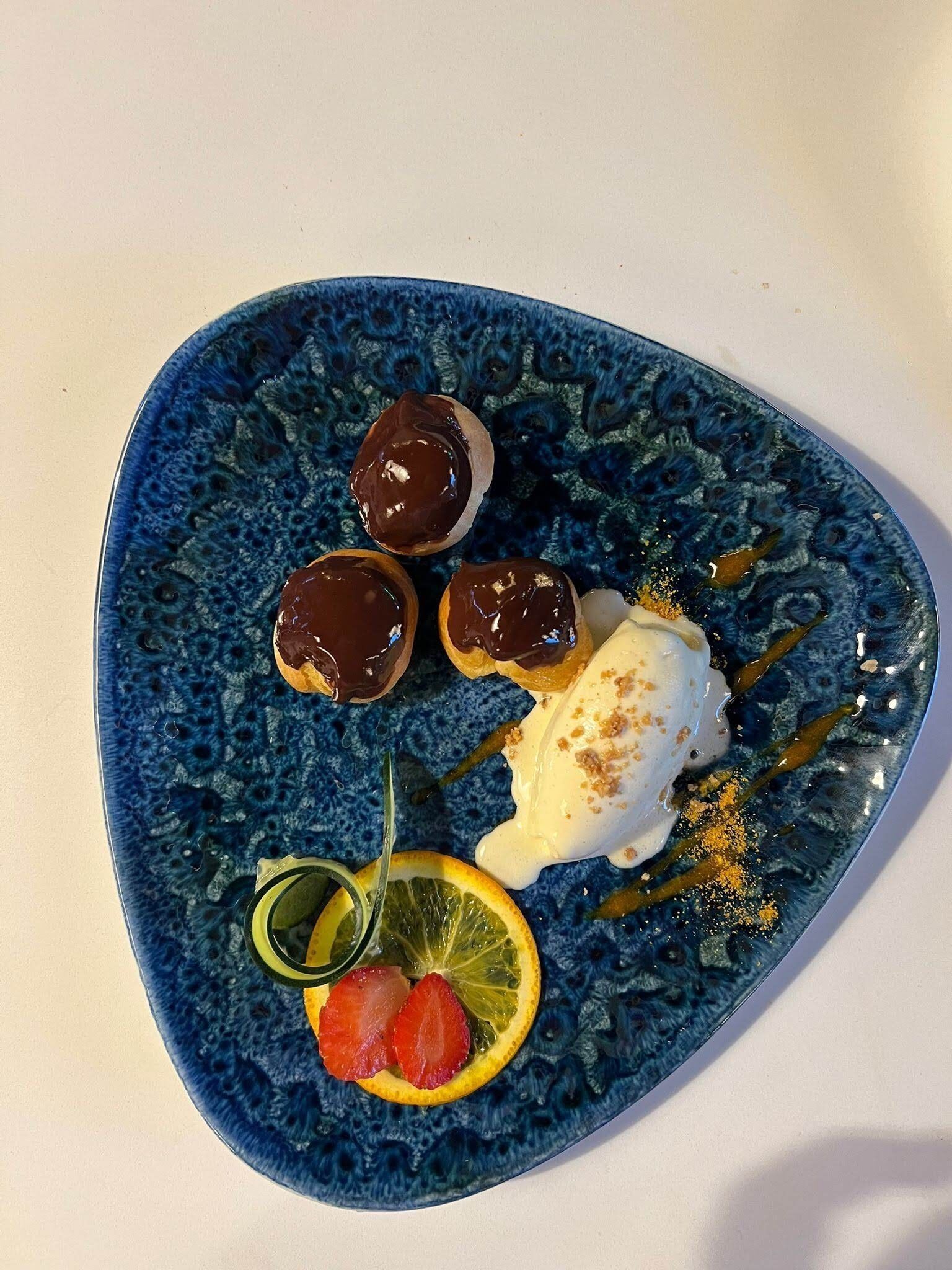 Un plato azul con cuatro postres bañados en chocolate y una bola de helado con un chorrito de jarabe y nueces espolvoreadas.