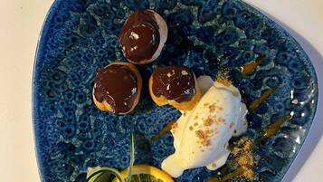 Un plato azul con cuatro postres bañados en chocolate y una bola de helado con un chorrito de jarabe y nueces espolvoreadas.