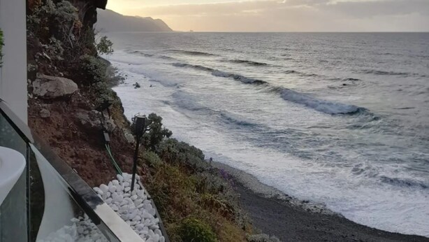 Une vue sur la côte, avec une falaise rocheuse et des vagues qui s’écrasent sur une plage de galets.