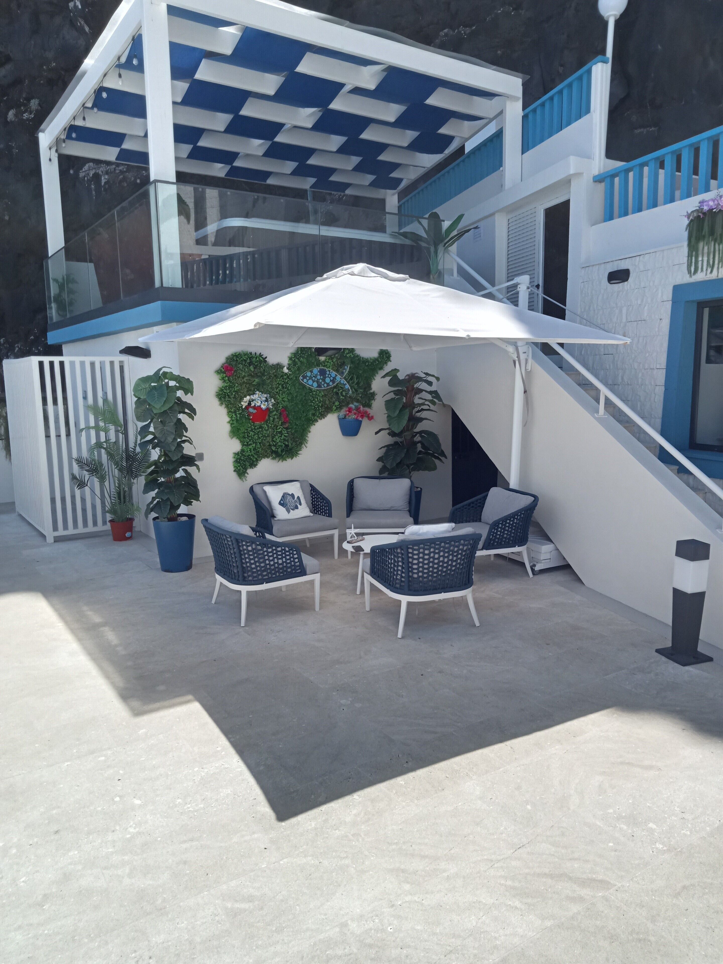 An outdoor patio area with a white umbrella, wicker chairs, and potted plants.