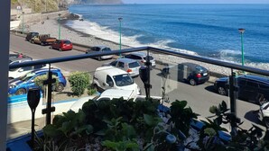Un balcon avec vue sur l’océan, un espace de stationnement et un bâtiment doté d’un toit en pente.