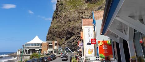 A coastal street with buildings, a cliff, and a view of the ocean.