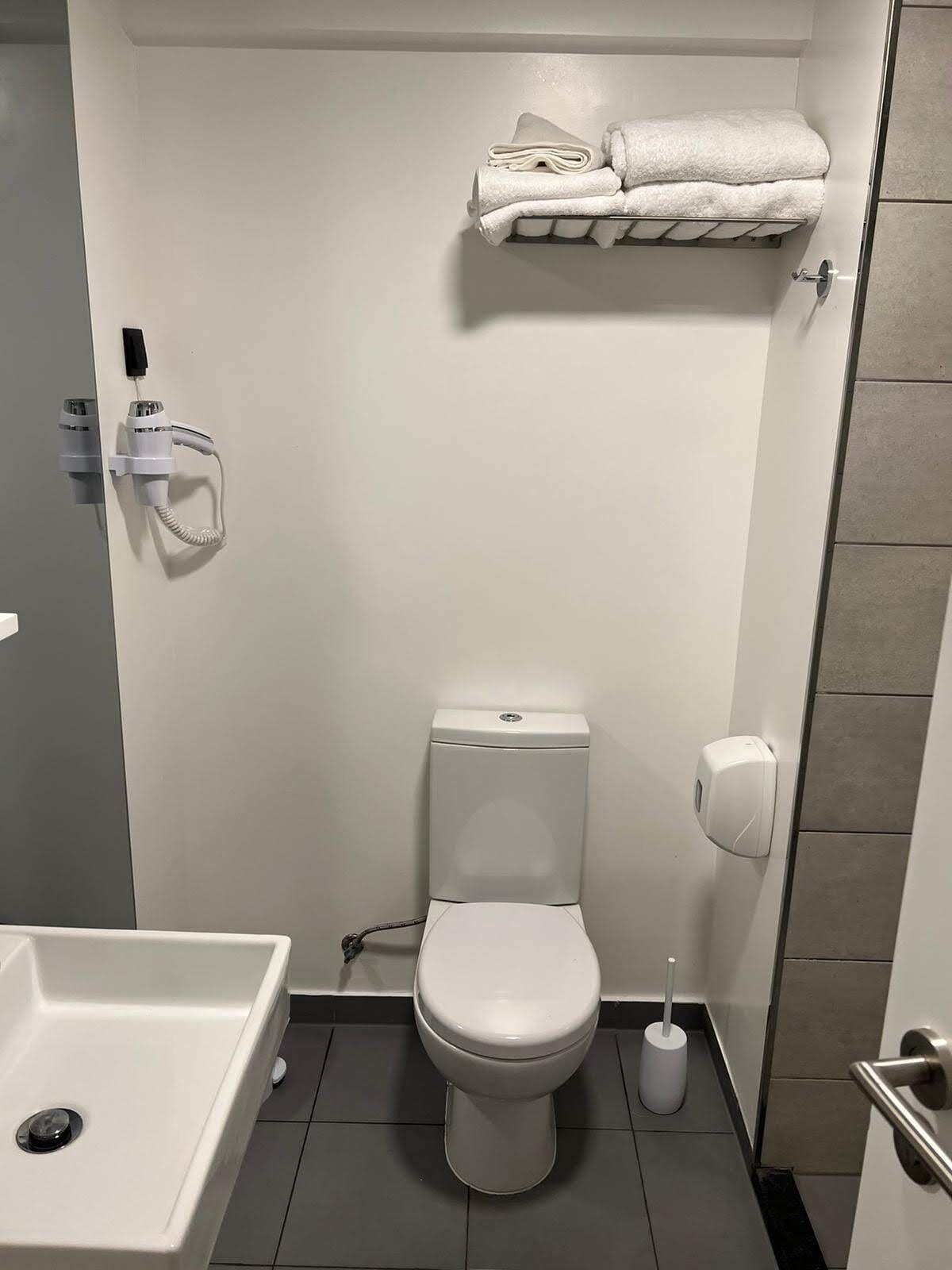 A small, modern bathroom with a toilet, a towel rack, a hand dryer, and a toilet paper holder.