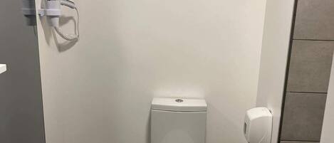 Un baño pequeño y moderno con inodoro, toallero, secador de manos y dispensador de papel higiénico.