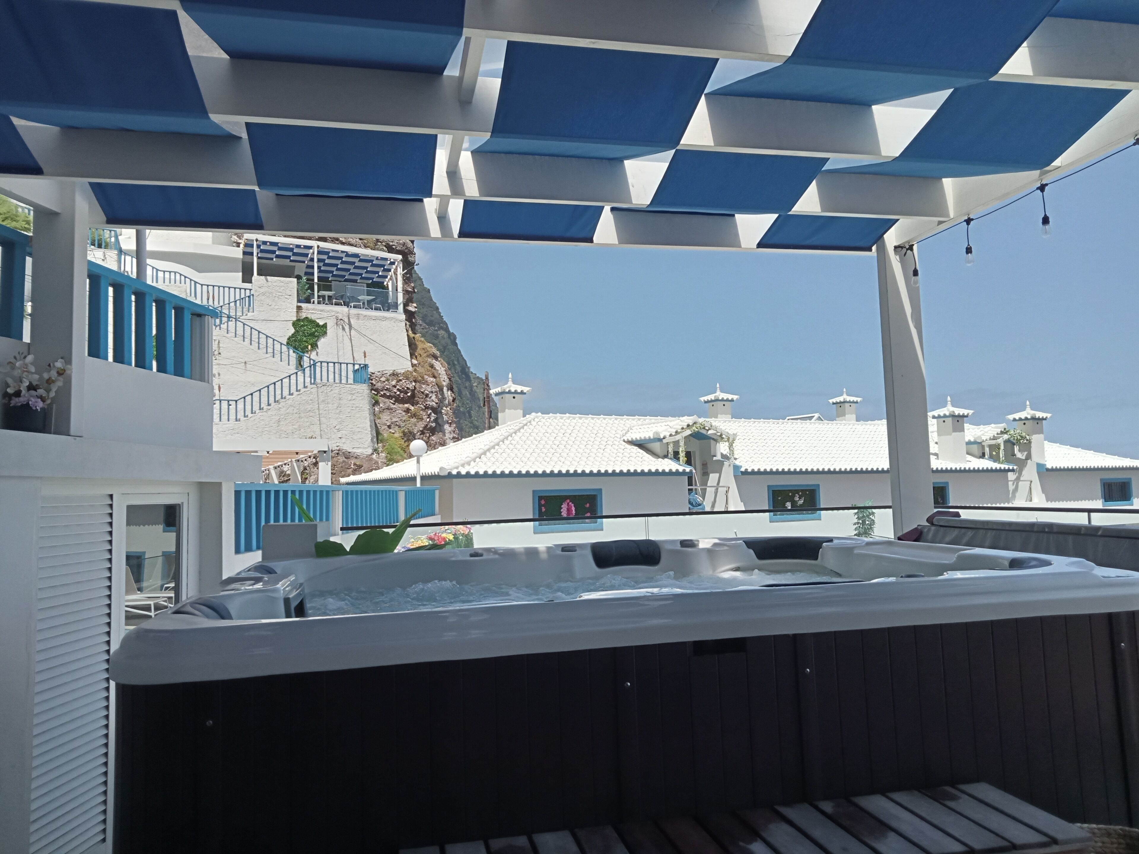 A hot tub area with a view of a white building with blue accents and a staircase leading to a cliff.