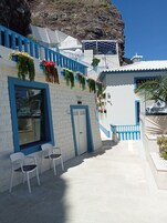 Un edificio con fachada blanca y detalles azules, que presenta una escalera con plantas colgantes y una puerta.