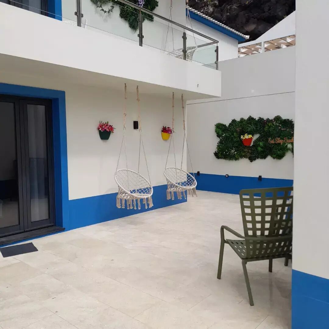 A spacious indoor area with a high ceiling, a blue and white color scheme, hanging macrame chairs, a green chair, and decorative plants.