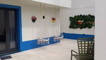 A spacious indoor area with a high ceiling, a blue and white color scheme, hanging macrame chairs, a green chair, and decorative plants.