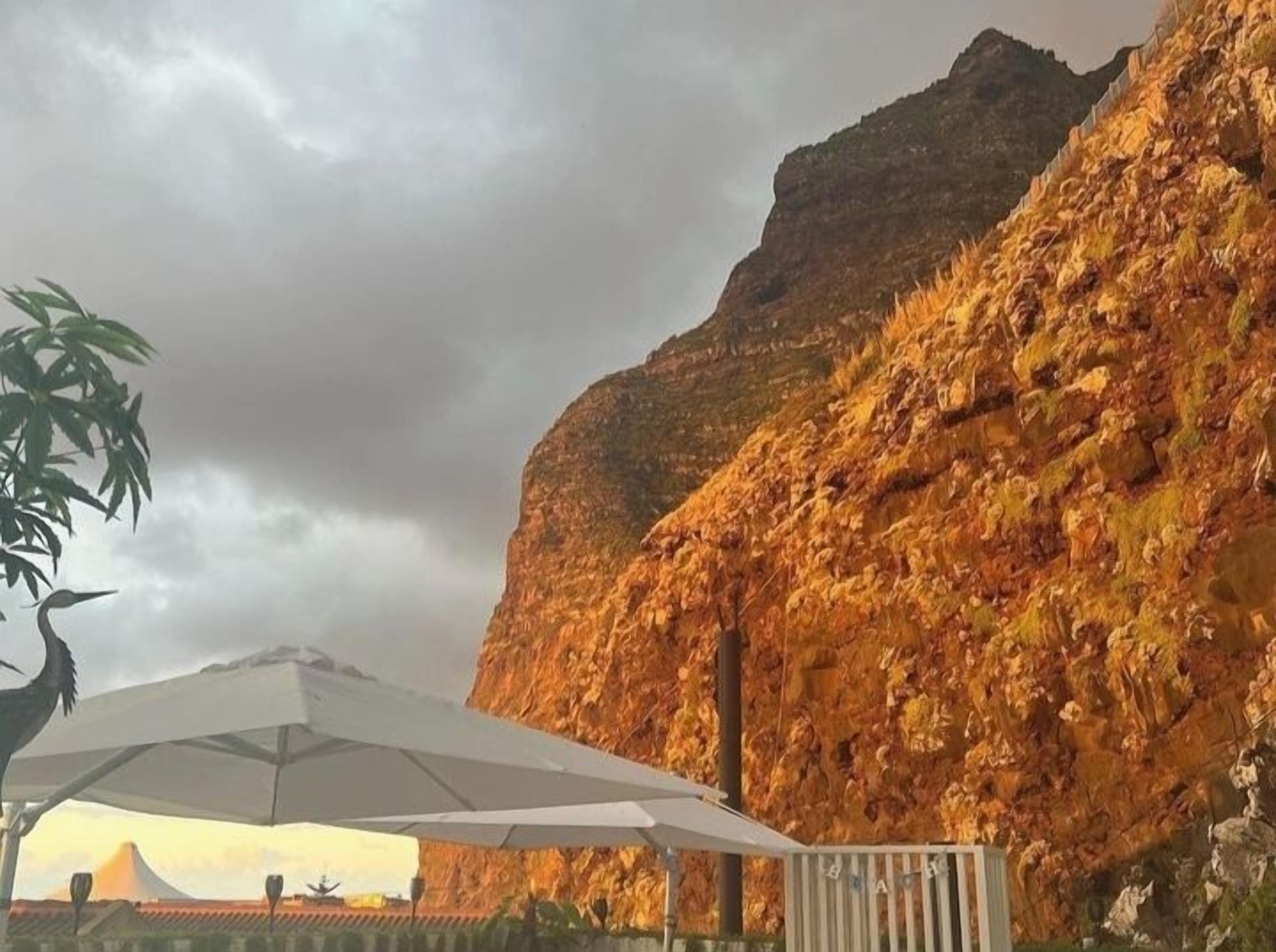Une falaise rocheuse avec un parasol blanc et une statue d'oiseau au premier plan.
