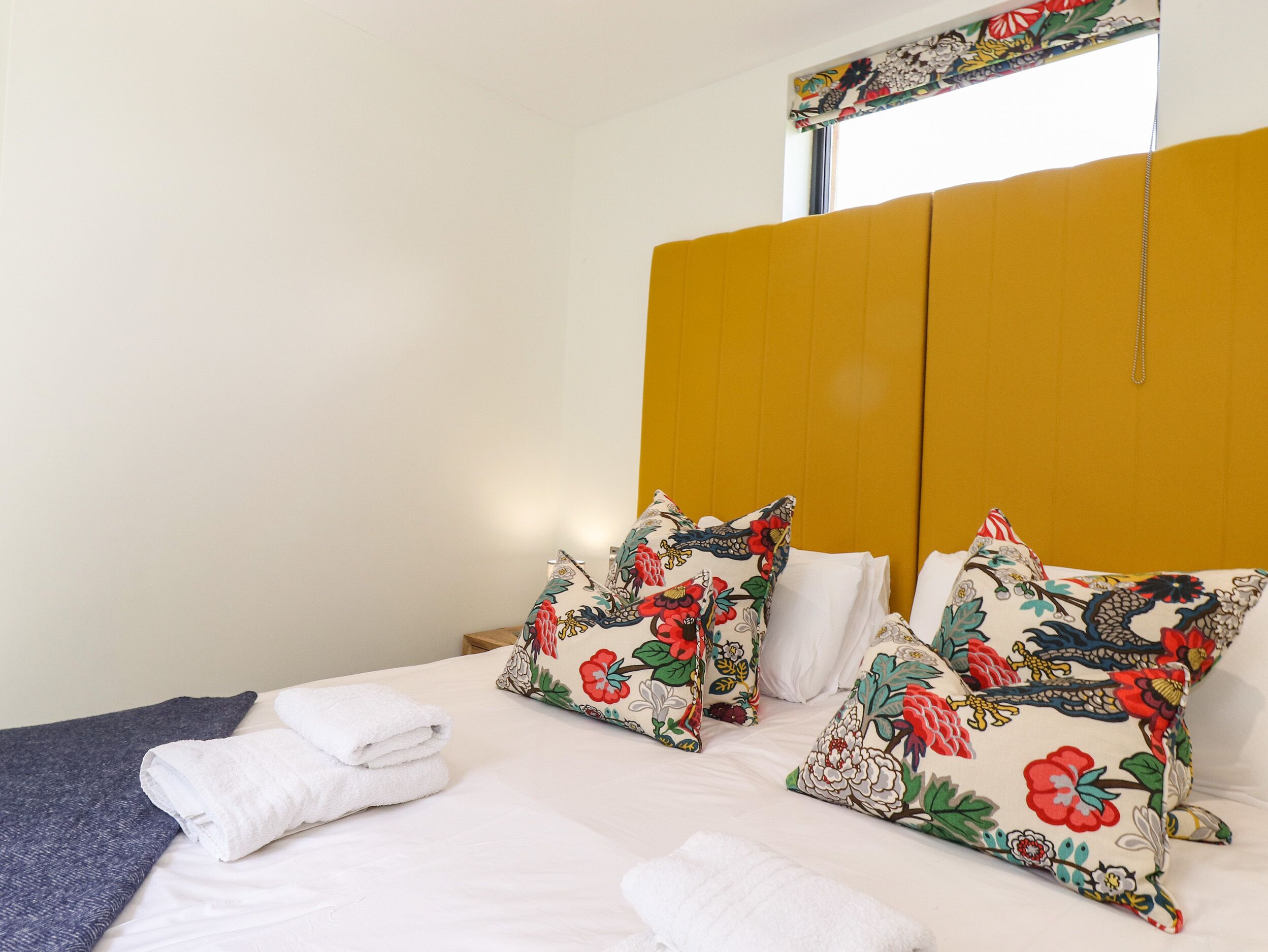 Ein Bett mit weißer Bettwäsche, Kissen mit Blumenmuster und einem gefalteten Handtuch.