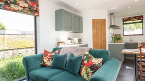 A modern living room with a green sofa, a wooden door, and a kitchen area with a microwave and sink. - Brow Wood Cabin (Penrith)