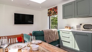 A modern kitchen with a flat-screen TV, a dining area with a wooden table set for two, and a cozy seating area with a green sofa. - Brow Wood Cabin (Penrith)