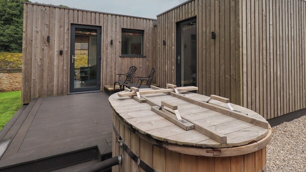 A modern wooden building with a deck and outdoor seating area. - Brow Wood Cabin (Penrith)