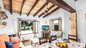 A cozy living room with a wooden ceiling, a television, a dining table with a fruit bowl, and a sofa with cushions. - Casita Fontxica - Two Bedroom Villa, Sleeps 4 (Mallorca)