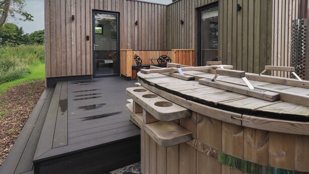 A modern wooden cabin with a deck, a hot tub, and a door leading to an interior space. - Bluebell Cabin (Penrith)