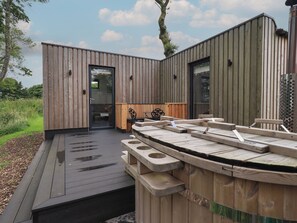 A modern wooden cabin with a deck, a hot tub, and a door leading to an interior space. - Bluebell Cabin (Penrith)