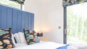 A hotel room with a bed, pillows, a lamp, and a view of trees through the window. - Bluebell Cabin (Penrith)