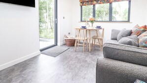 A modern living room with a sofa, a dining table with chairs, and a TV mounted on the wall. - Bluebell Cabin (Penrith)