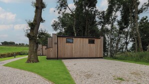 A modern wooden cabin with a gravel driveway and a grassy area. - Bluebell Cabin (Penrith)