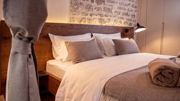 Siististi pedattu sänky, jossa on puinen pääty, kuvioitu seinävaate ja yöpöydällä oleva lamppu.
