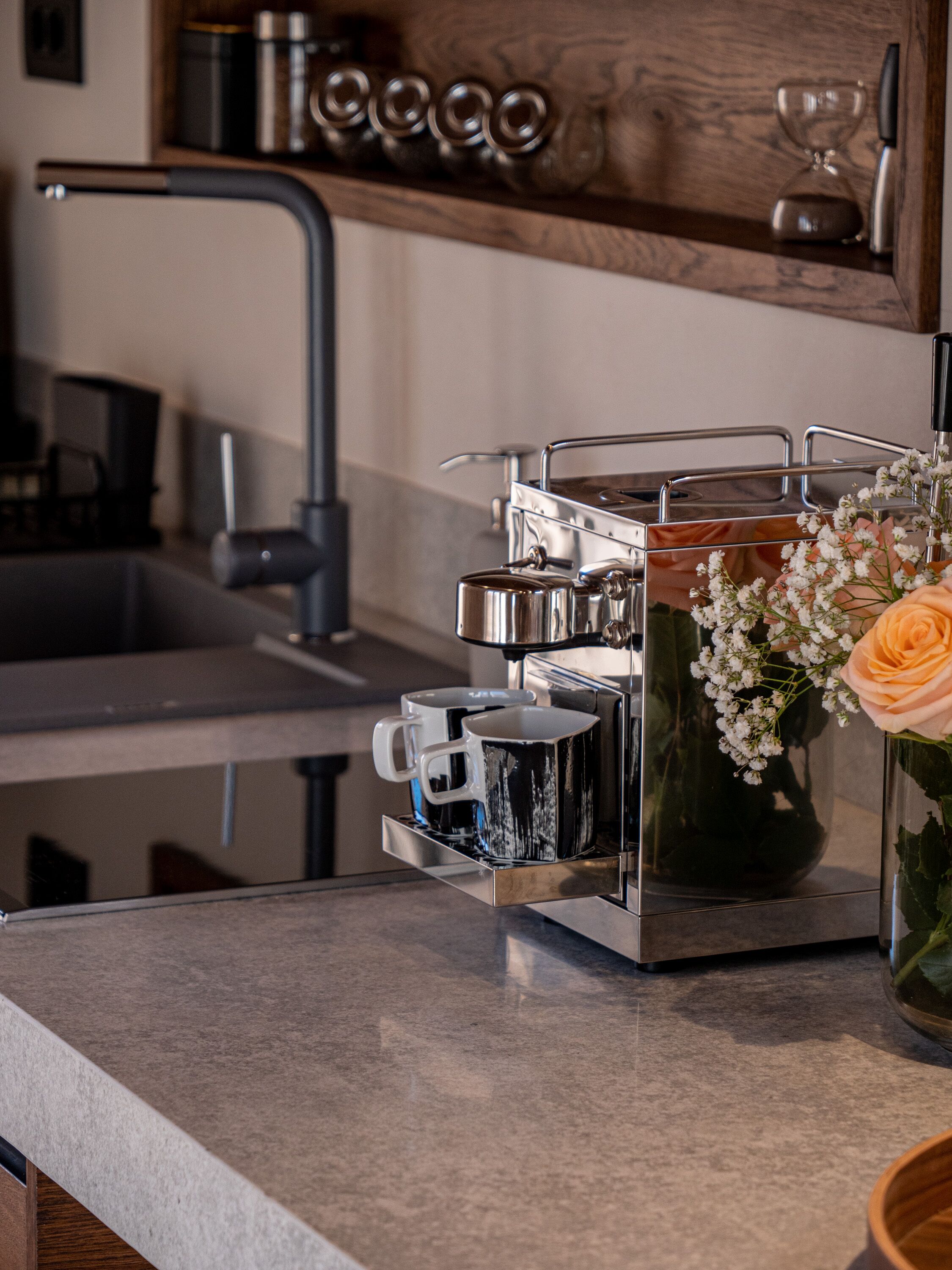 A kitchen with a coffee machine, a sink, and a vase with flowers.