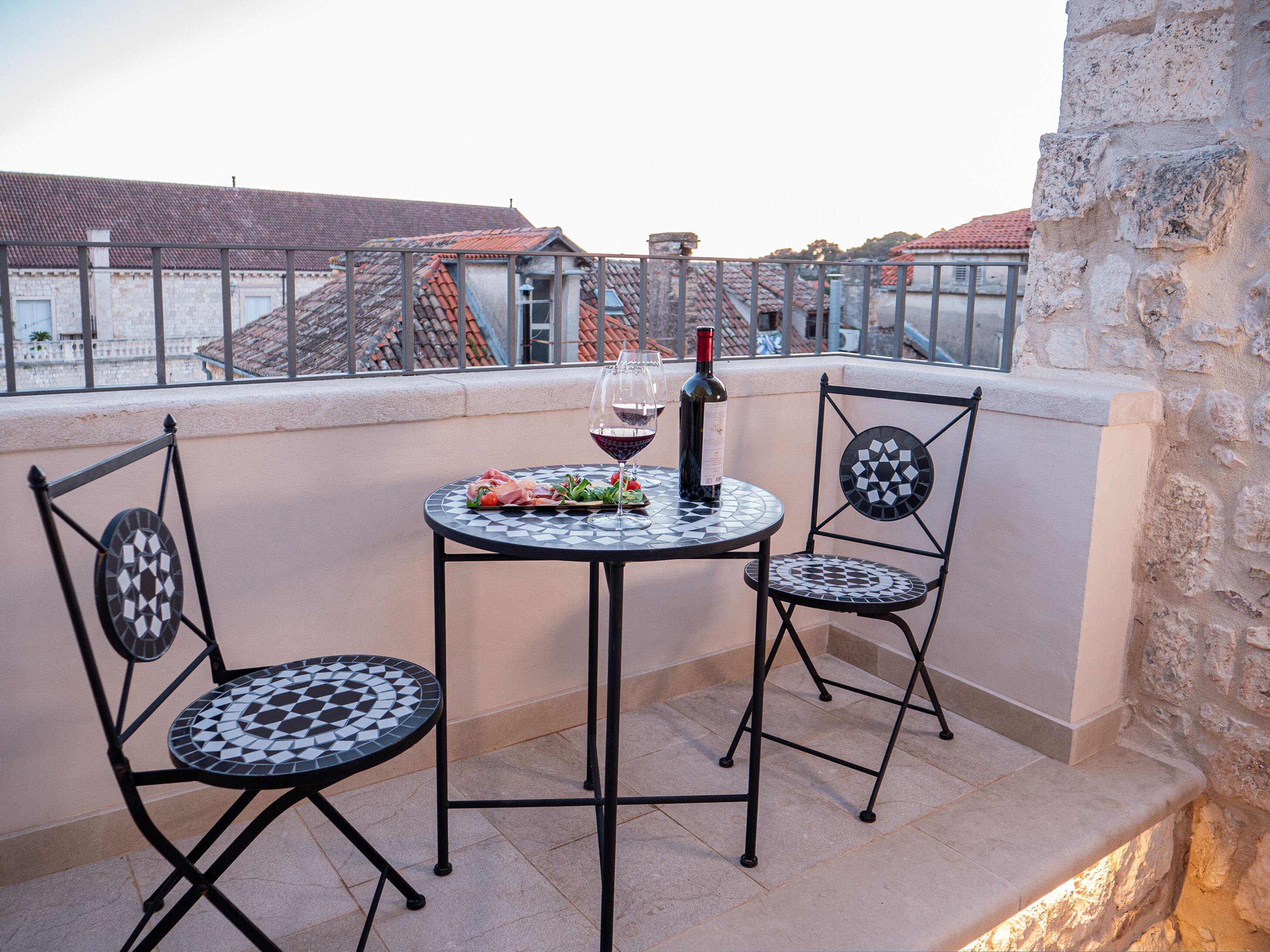 A balcony with two chairs and a table, a bottle of wine, and a plate of food.