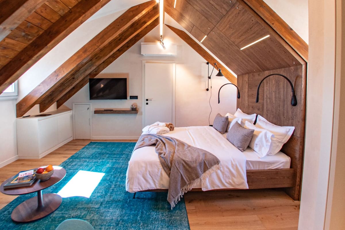 A cozy attic bedroom with a sloped ceiling, a bed with pillows, a bedside table, and a TV.