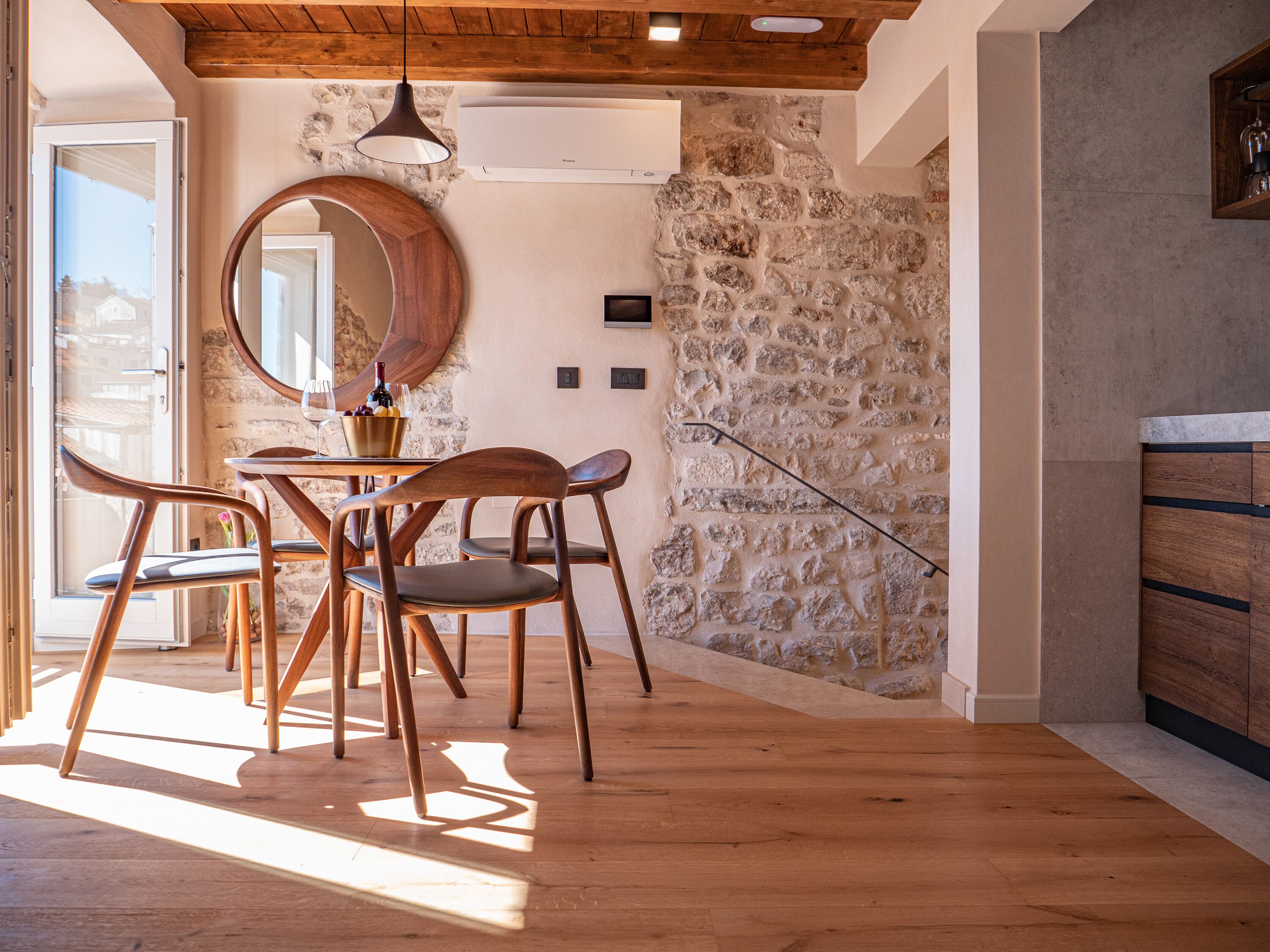 A dining area with wooden chairs, a round table, and a stone wall.
